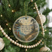 A round ornament hanging on a Christmas tree, featuring a scenic landscape with a lighthouse and a path leading through the greenery.