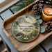 A wooden tray with a decorative ornament featuring a scenic landscape of Metamora-Hadley Recreation Area, Michigan, and a candle.