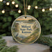 A round ornament with a painting of Milford State Park, Kansas, featuring a lighthouse, a boat, and a bird, hanging on a string.