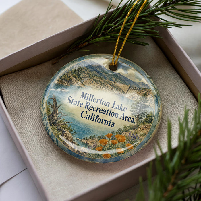 A decorative ornament in a box, featuring a scenic landscape with mountains, water, and pine trees.