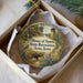 A decorative ornament in a box, featuring a scenic landscape with a bird, a castle, and a path leading to a waterfall.