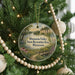 A round ornament hanging on a Christmas tree, featuring a scenic landscape with a path, bridge, and water.