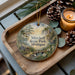 A wooden tray with a decorative ornament featuring a scenic landscape of Mitchell State Park, Michigan, and pine cones.