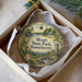 A decorative ornament in a box, featuring a scenic landscape with a castle, trees, and a lake.