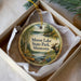 A circular ornament with a moose and a canoe, surrounded by a scenic landscape of trees and a lake, is displayed in a box.