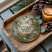 A decorative ornament featuring a scenic landscape of Morison-Rockwood State Park, Illinois, with a bridge and pine cones on a wooden tray.