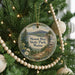 A round ornament hanging on a Christmas tree, featuring a scenic landscape with mountains and pine trees.