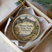 A decorative ornament in a box, featuring a scenic landscape with mountains, trees, and a small building.
