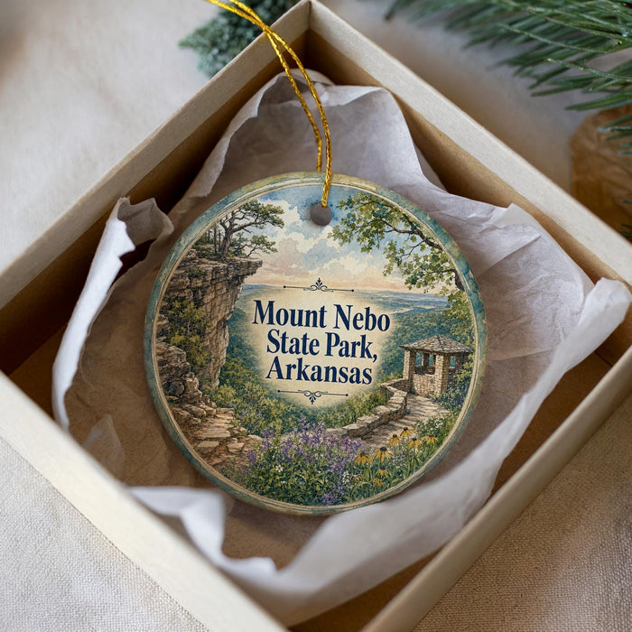 A decorative ornament in a box, featuring a scenic landscape with a house and trees, with the text "Mount Nebula State Park, Arkansas" printed on it.