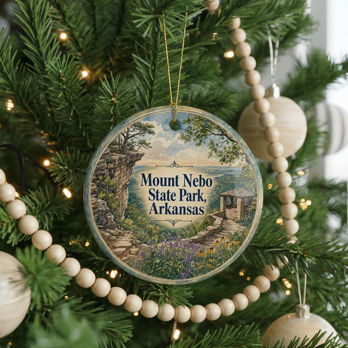 A round ornament hanging on a Christmas tree, featuring a scenic landscape with a path leading to a cliff and a body of water.