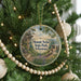 A round ornament hanging on a Christmas tree, featuring a scenic landscape with a path leading to a cliff and a body of water.