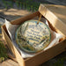 A decorative ornament in a box, featuring a scenic landscape with mountains, trees, and a waterfall.