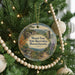 A round ornament on a Christmas tree, featuring a scenic landscape with a castle, trees, and a body of water.