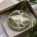 A decorative ornament in a box, featuring a scenic image of Muskallon Lake, State Park, Michigan.