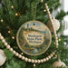A round ornament hanging on a Christmas tree, featuring a lighthouse and a scenic landscape.