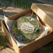 A decorative ornament in a wooden box, featuring a scenic landscape with a waterfall and forest.