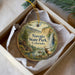 A decorative ornament in a box, featuring a scenic landscape with a waterfall, a cabin, and a deer.