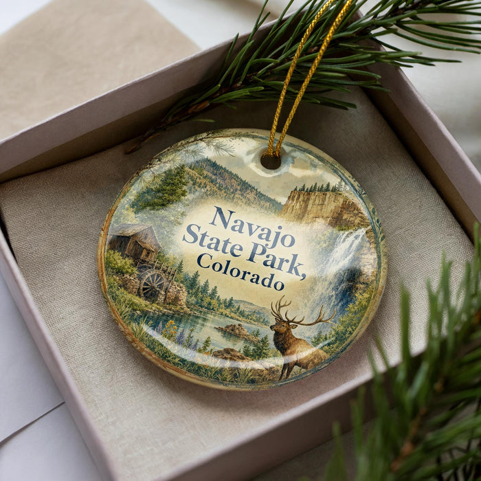 A decorative ornament in a box, featuring a scenic landscape with mountains, a river, and a deer.