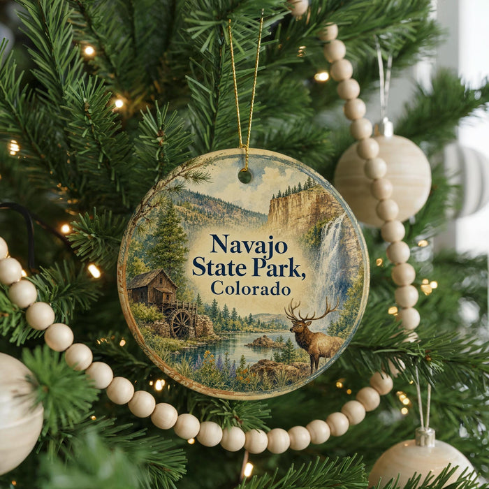 A round ornament hanging on a Christmas tree, featuring a scenic landscape with a waterfall and a deer.