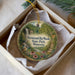 A decorative ornament in a box, featuring a scenic image of a waterfall surrounded by lush greenery and colorful flowers.