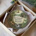 A decorative ornament in a box, featuring a scenic landscape with a river, trees, and a building.
