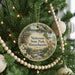 A round ornament hanging on a Christmas tree, featuring a scenic landscape with a castle, trees, and a stream.