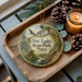 A decorative ornament with a scenic image of Nine Eagles State Park, Iowa, is displayed on a wooden tray alongside pine cones and a lit candle.