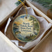 A decorative ornament in a box, featuring a scenic image of a lake, a bird, and a sunset.