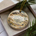 A decorative ornament with a desert landscape and a vehicle, placed inside a box with pine branches.