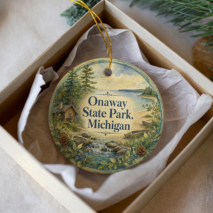 A circular ornament with a scenic landscape of Onaway State Park, Michigan, displayed in a box with a white tissue paper lining.