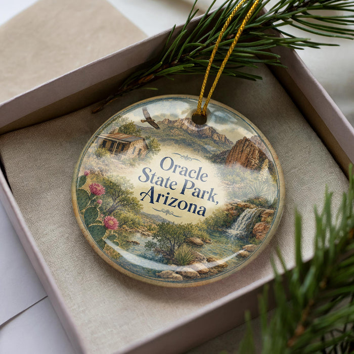 A decorative ornament with a landscape scene featuring a house, mountains, and a waterfall, placed inside a box with pine branches.