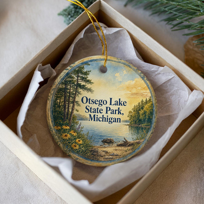 A decorative ornament in a box, featuring a scenic landscape with a lake, trees, and a sunset.