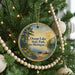 A round ornament hanging on a Christmas tree, featuring a scenic landscape with a lake and trees.