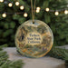 A decorative ornament featuring a scenic landscape with mountains, trees, and a stream, hanging in front of a Christmas tree with twinkling lights.