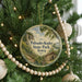 A round ornament hanging on a Christmas tree, featuring a scenic landscape with a path leading to a cabin.