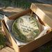 A wooden box containing a decorative ornament with a scenic landscape of Palisades-Kepler State Park, Iowa.