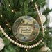 A round ornament hanging on a Christmas tree, featuring a scenic image of palm trees, a bird, and a body of water.