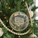 A round ornament hanging on a Christmas tree, featuring a scenic landscape with mountains, pine trees, and a pine cone.