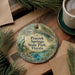 A decorative ornament featuring a peacock and the text "Peacock Springs State Park, Florida" is displayed on a wooden surface, accompanied by a cup of coffee and pine branches.