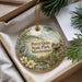 A decorative ornament with a bird and flowers, hanging from a string, placed inside a box with pine branches.