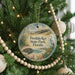 A round ornament hanging on a Christmas tree, featuring a beach scene with a bird and a turtle.
