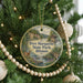 A round ornament hanging on a Christmas tree, featuring a scenic image of a park with a river and a cabin.