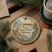 A decorative ornament with a scenic image of Perry State Park, Kansas, is displayed on a wooden surface alongside a cup of coffee and some pine branches.