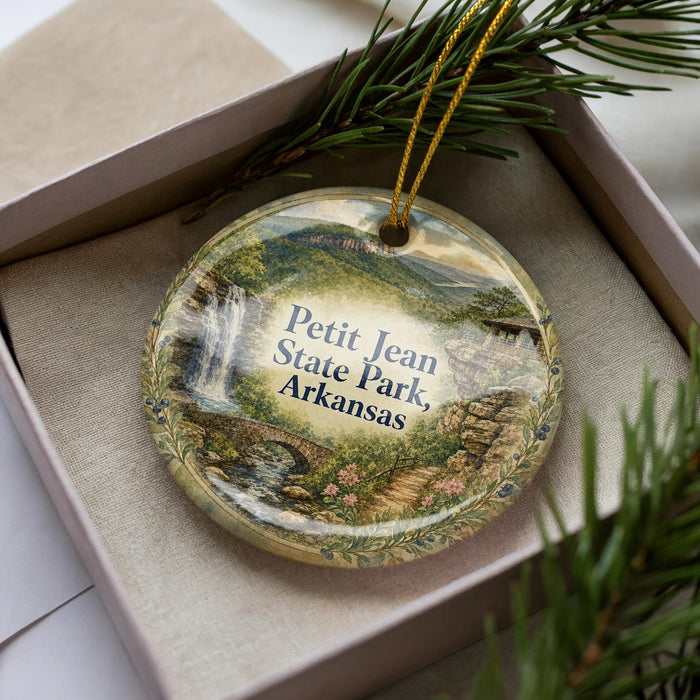 A decorative ornament in a box, featuring a scenic landscape with a waterfall and mountains, with the text "Petit Jean State Park, Arkansas" printed on it.