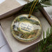 A decorative ornament in a box, featuring a scenic landscape with a waterfall and mountains, with the text "Petit Jean State Park, Arkansas" printed on it.