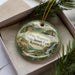 A decorative ornament with a scenic image of Pine Mountain State Resort Park, Kentucky, displayed in a box with pine branches.