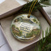 A decorative ornament in a box, featuring a scenic landscape with mountains, trees, and a bird, along with the text "Pinnacle Mountain State Park, Arkansas".