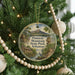A round ornament hanging on a Christmas tree, featuring a scenic landscape with mountains, trees, and a bird.