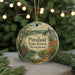 A round ornament with a scenic forest landscape and a bird perched on a tree, hanging from a string.