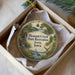 A circular ornament with a scenic landscape and wildlife, including a deer, is displayed in a box.